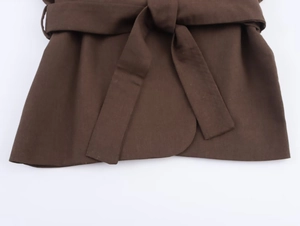 Detail of a brown linen wrap top featuring a waist tie bow and pleated texture
