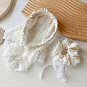 Detail of cream white lace headband with scalloped edges and pearl accents on white tray