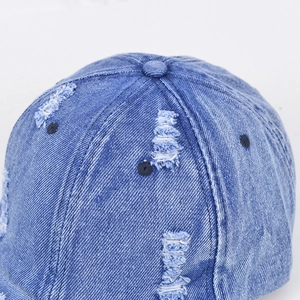 Close-up of distressed blue denim baseball cap showing heavy wash and ripped details