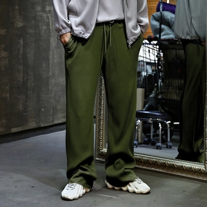 Detail view of olive green wide-leg trousers featuring unique vertical pleated texture