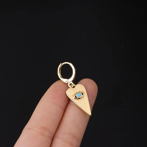 Detail of gold heart hoop earring with blue evil eye pendant held by hand