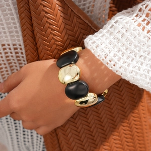 Gros plan du bracelet à maillons ovales en acrylique noir et or sur le poignet du mannequin