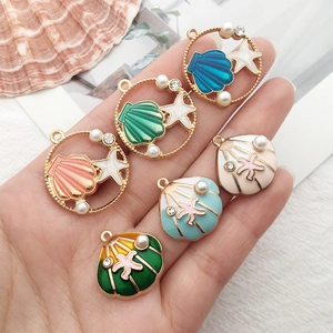 Macro shot of colorful enamel starfish and shell charms with pearls held in hand