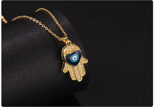 Macro shot of gold Hamsa hand pendant with blue heart evil eye and white zircon details