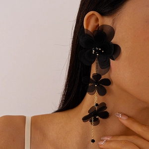 Dettaglio di lunghi orecchini a fiori in chiffon nero con nappe dorate sul modello