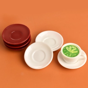 Miniature dollhouse coffee set with red and white saucers and a latte cup on orange background