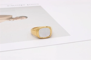 Détail de l'incrustation en nacre sur une bague chevalière dorée avec fond de magazine