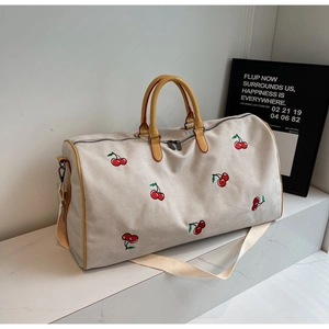 Dettaglio della borsa da viaggio in tela vintage con ricamo ciliegia e manici gialli