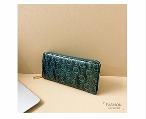 Detail of dark green embossed long wallet with gold hardware on a desk setting