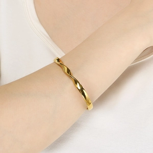 Detail shot of a twisted 18K gold-plated stainless steel wavy bangle on a model wrist