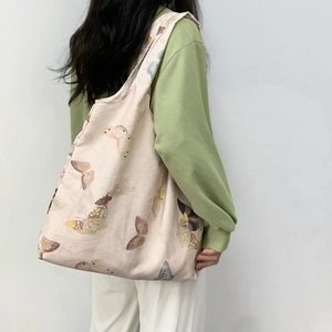 Close-up of beige canvas tote bag with butterfly print worn by a model in soft lighting