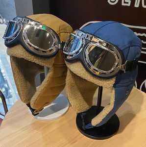Dettaglio dei cappelli da aviatore marroni e blu con fodera in pile e occhiali protettivi