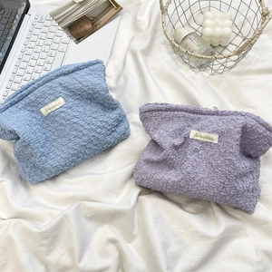 Close-up of blue and purple bubble textured cosmetic bags on a white bedding background
