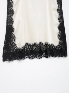 Close-up of cream satin fabric with detailed black lace trim on the garment hemline