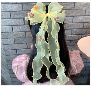 Detail of yellow organza bow hair clip with floral embroidery and long ribbons for girls