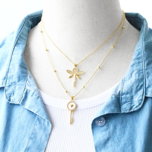 Close-up of double-layer gold necklace featuring a dragonfly and heart key pendant