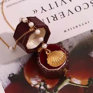 Detailed view of 18K gold shell pendant necklace with pearls in a red jewelry box