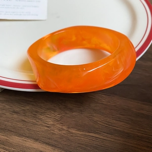 Detailed view of an orange marbled acrylic bangle resting inside a vintage ceramic plate