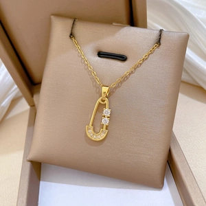 Detailed view of a gold safety pin pendant necklace with zircon on a beige cushion