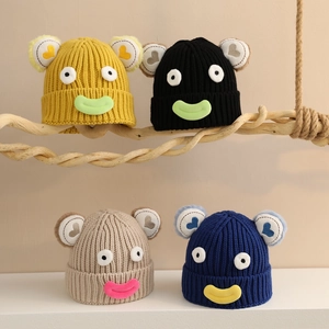 Détail de bonnets en grosse maille avec yeux de dessin animé et patchs grande bouche