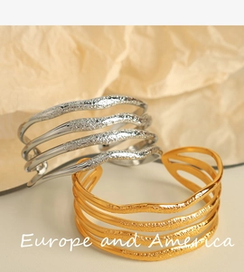 Detail of 18K gold and silver wide hammered wave texture bangles on warm background
