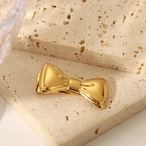 Detailaufnahme einer goldenen Haarklammer in Schleifenform auf Travertin-Hintergrund