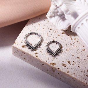 Silver V-shaped G23 titanium nose ring with decorative bead on a rustic stone base