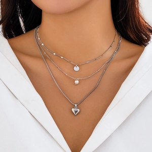Detail of layered silver necklaces with heart charms and pearl accents on a model