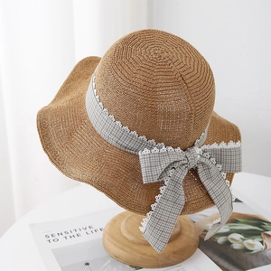 Detailed view of a brown straw sun hat featuring a grey plaid bow and white lace trimming