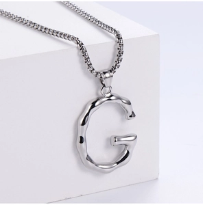 Detailed view of stylized letter G pendant on silver box chain over white background