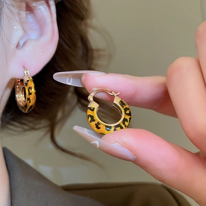 Close-up of 14k gold plated leopard print hoop earrings worn on ear with metal details
