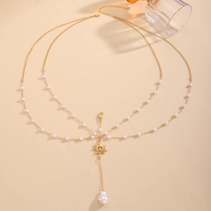 Close-up of golden body chain featuring white pearls and a sun pendant with shell drop