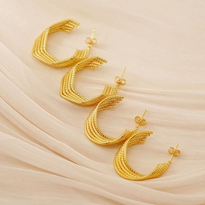 Close-up of four gold twisted hoop earrings with a glossy finish on beige fabric