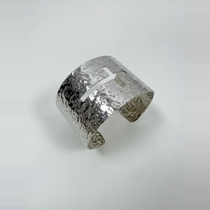 Close-up of hammered silver cuff bracelet featuring a textured hollow cross design