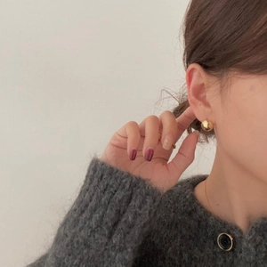 Close-up of minimalist polished gold sphere earrings worn with a grey knit sweater