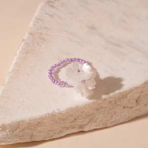 Detailed view of handmade beaded flower ring with purple beads and white floral cluster