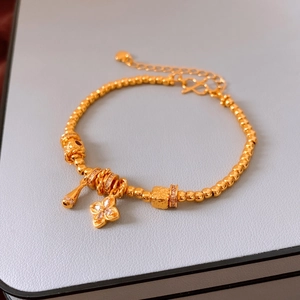 Detail of 24K gold-plated beaded bracelet with floral and clover charms on leather texture