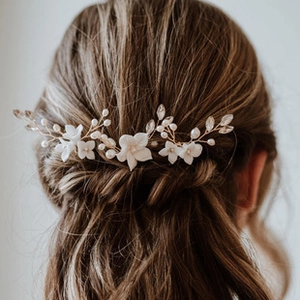 Detailed close-up of bridal hair band with white ceramic flowers and pearls on brown hair