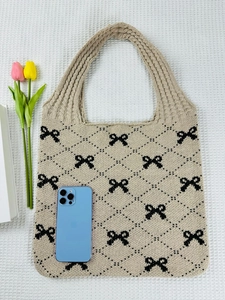 Detail of beige knitted tote bag with black bow patterns next to a phone for scale