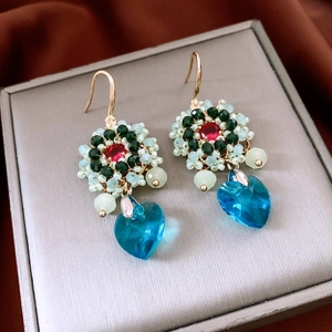 Detail of handmade beaded flower earrings with blue heart crystal on a jewelry box