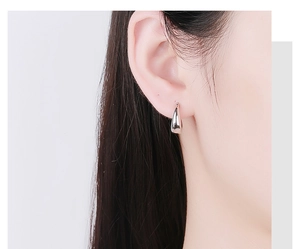 Close-up of minimalist silver oval drop earrings worn to show elegant style