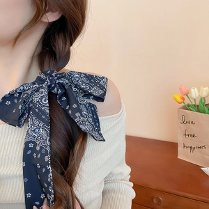 Detail of a dark blue paisley floral scarf tied as a large bow on a side braid hairstyle