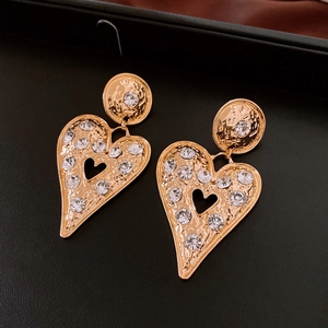 Close-up of golden heart earrings with hammered texture and sparkling crystals on black leather