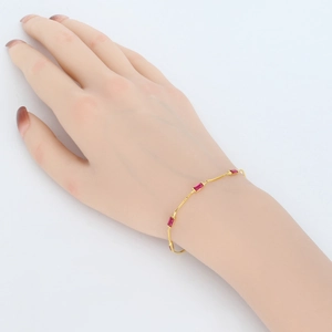 Detail of elegant gold bracelet featuring small rectangular red gemstones on a fine chain