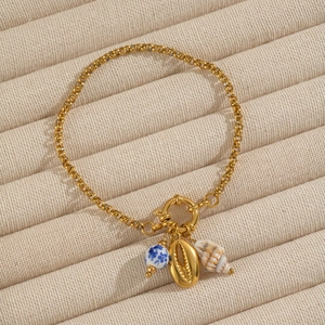 Detail view of a gold chain bracelet with ceramic bead and seashell charms on velvet tray