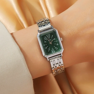 Detail of silver rectangular quartz watch with green dial on luxury gold satin background