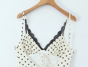 Dettaglio dello scollo a V con pizzo e motivo a pois su un abito bianco a spalline