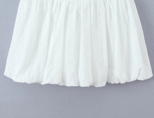 Detail of white dress hem featuring delicate floral embroidery and textured pleated fabric