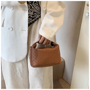 Chic brown woven pillow bag held by model in white suit on stairs, lifestyle detail