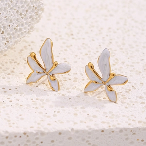 Macro view of gold-plated white enamel butterfly stud earring on a white coral texture